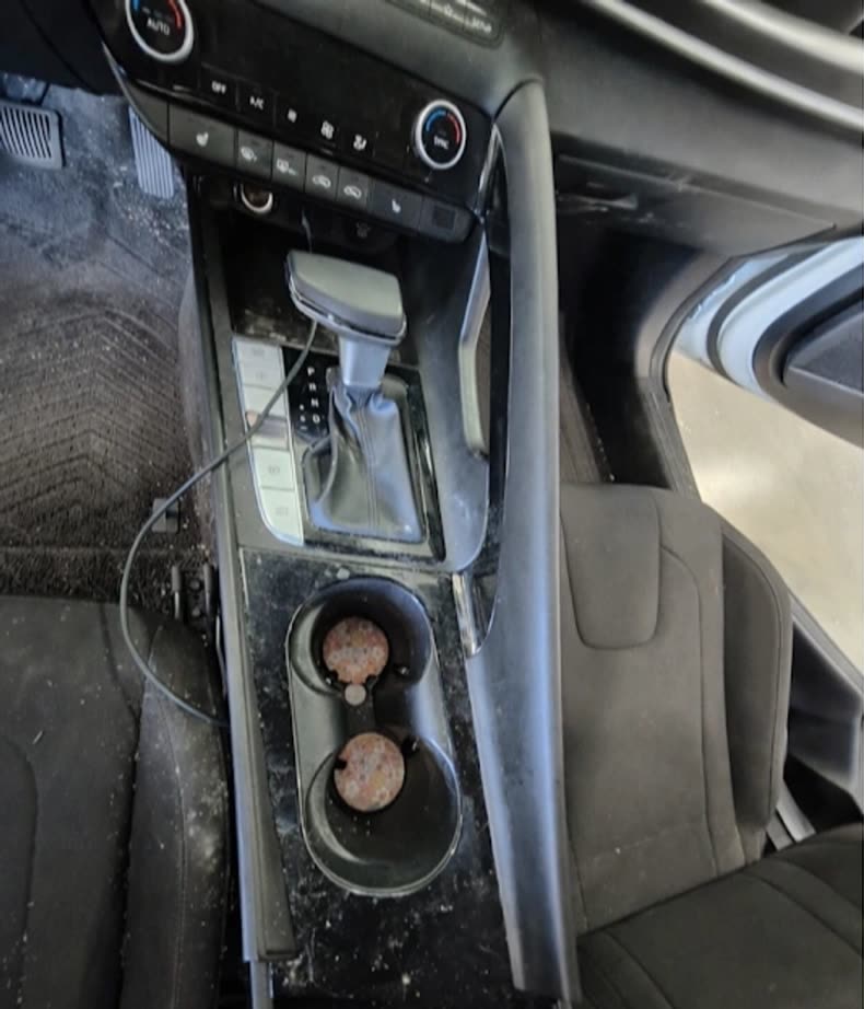 A car center console before an interior deep clean — stained cup holders, dusty trim and marked seats
