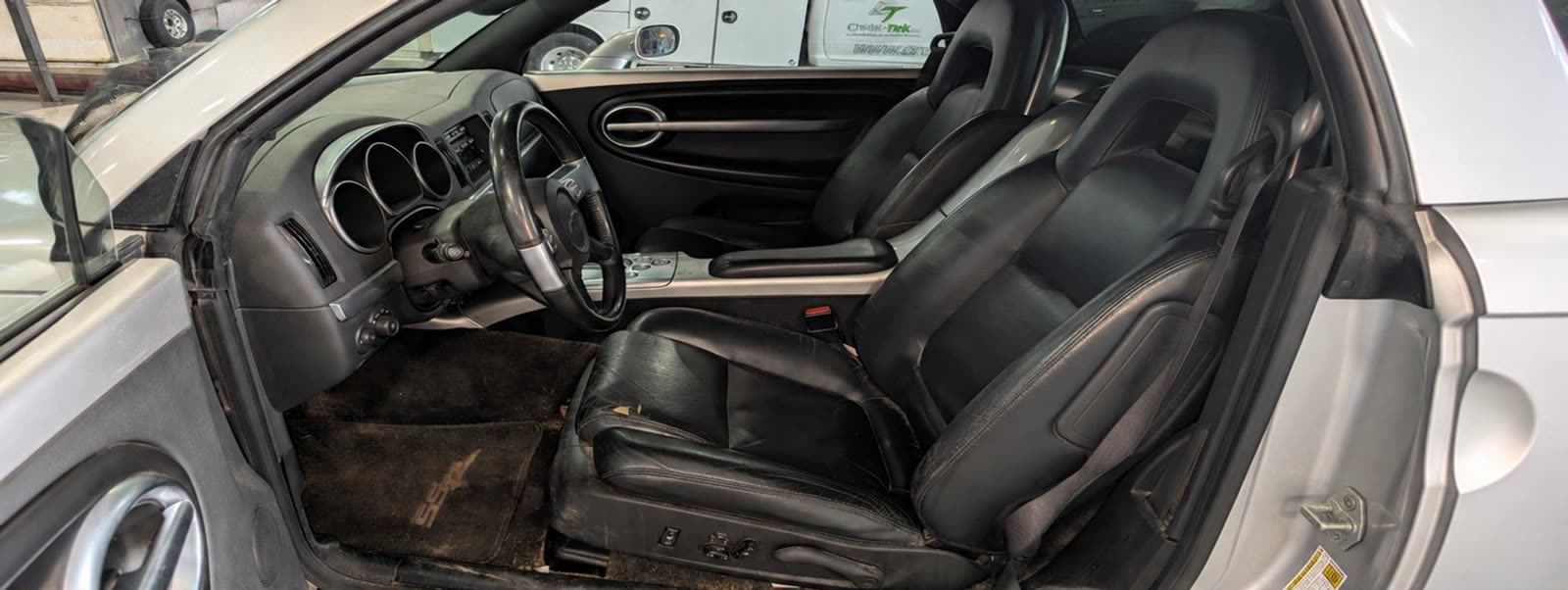 A convertible's leather interior before cleaning — dirty carpet and dull, worn-looking seats