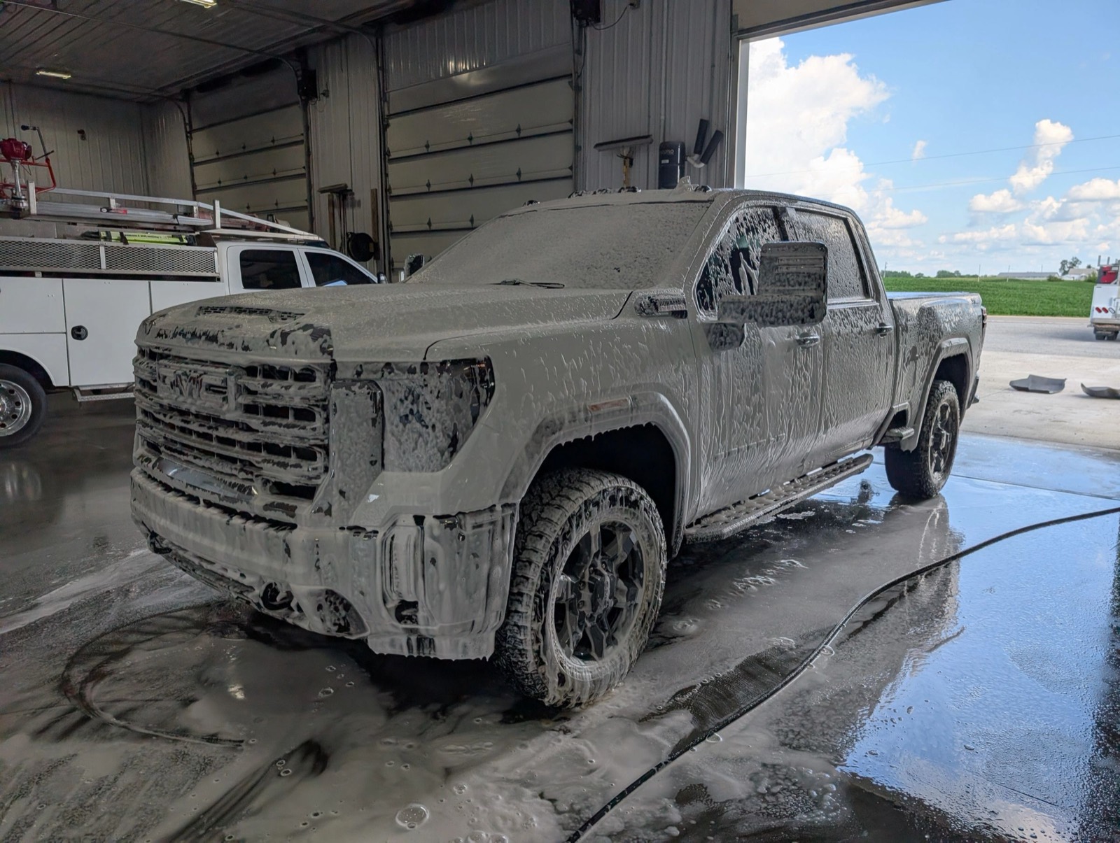 A GMC pickup covered in white foam during a hand wash inside the Signature Auto Detailing shop bay
